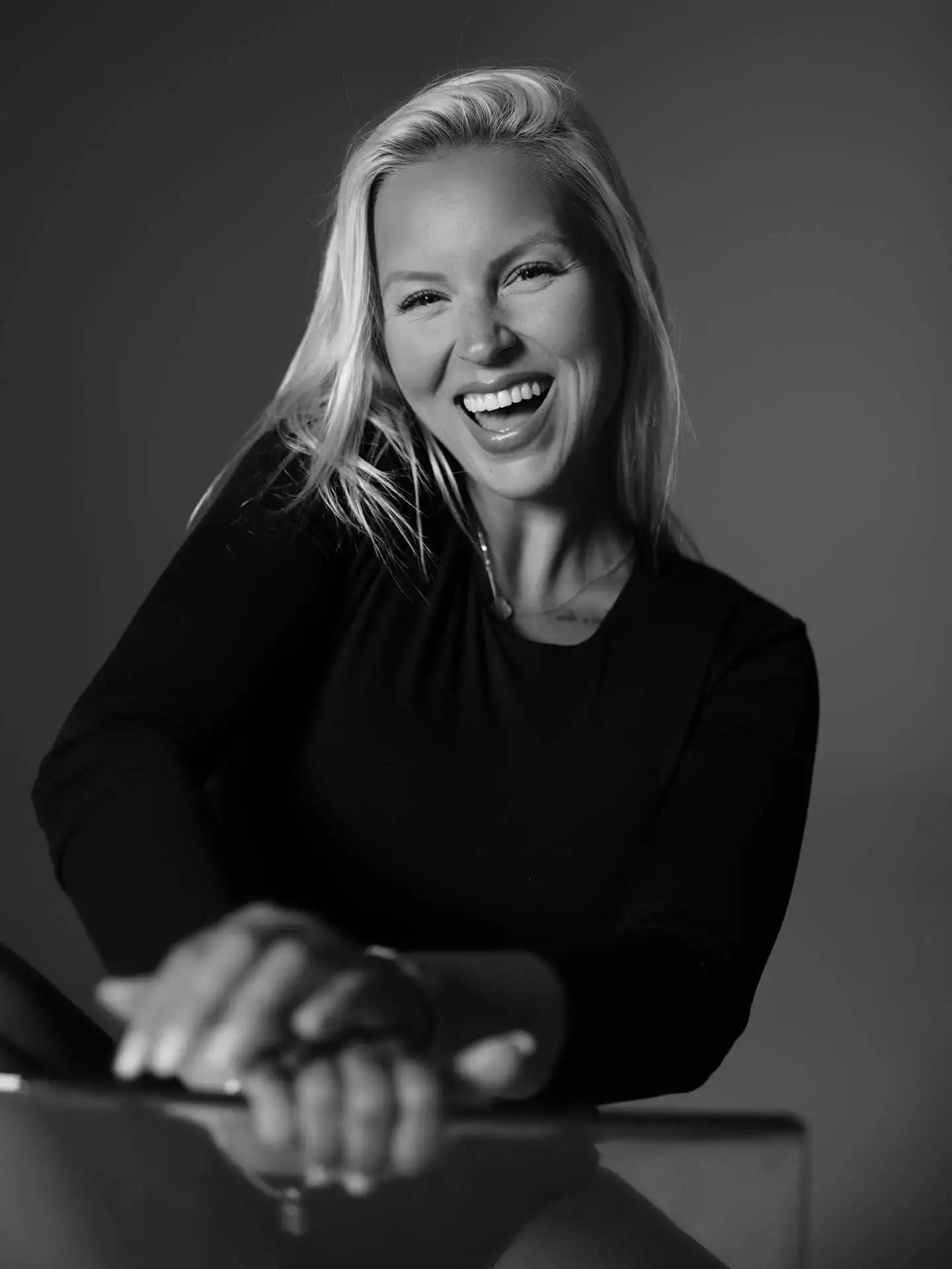 Chosen By Ekaterina Black and white portrait of a smiling woman with long blonde hair, wearing a long-sleeved dark top, posed against a plain background—perfect for promoting female development or an inspiring women webinar. Women & Female Mentorship